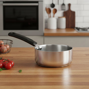 Stainless steel saucepan on a wooden kitchen counter with tomatoes and a basket of eggs.