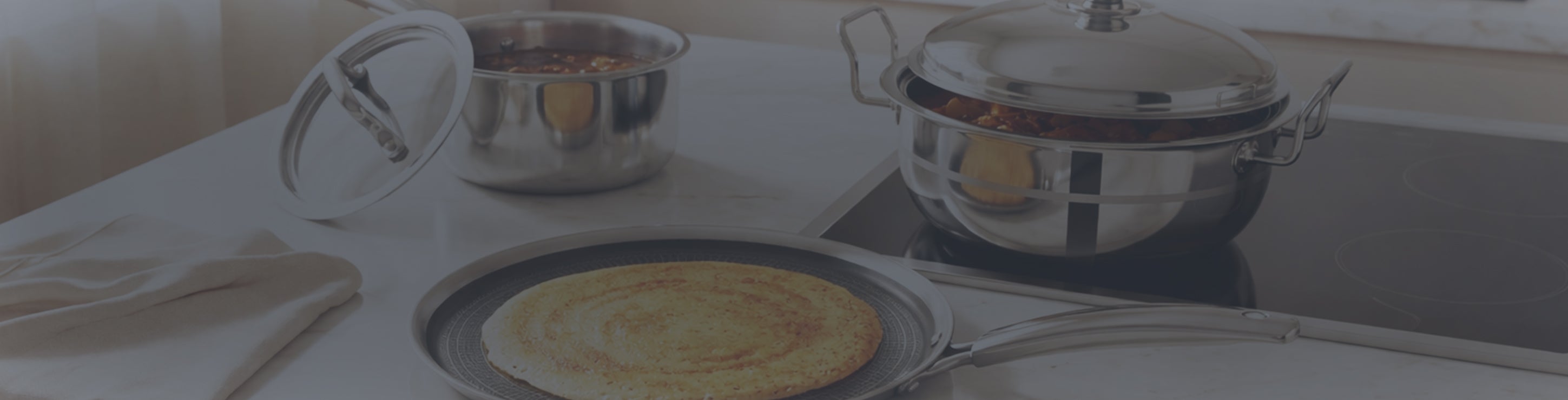 Stainless steel cookware set with dosa pan and cooking pots in a modern kitchen setup